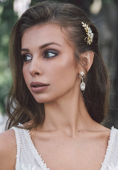 a woman with blue eyes wearing earrings and a white dress is looking off to the side