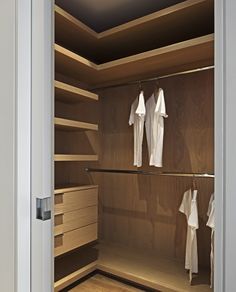 an open closet with clothes hanging from the ceiling and wooden shelves on both sides,