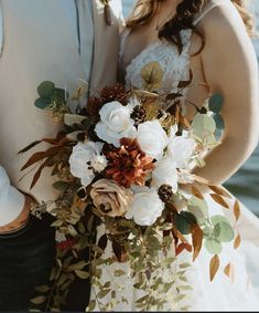 the bride and groom are standing close together by the water with their bouquets in hand