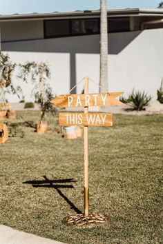 a wooden sign that says party this way in front of a building with palm trees