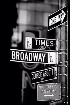 black and white photograph of street signs on a pole in front of a traffic light