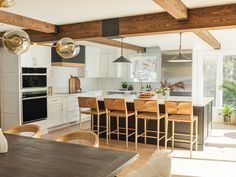 an open kitchen and dining room area with wood beams on the ceiling, white cabinets and counter tops