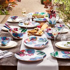 an outdoor table set with plates and wine glasses