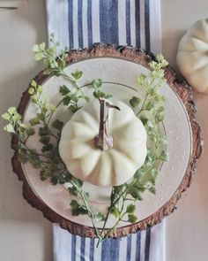 a white pumpkin sitting on top of a table next to a plate with flowers and leaves