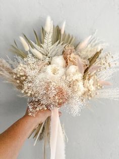 a person holding a bouquet with white flowers and feathers on it's side, in front of a gray wall