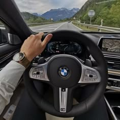 a man driving a bmw car on a road with mountains in the backgroud