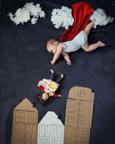 a baby is laying on the ground next to some paper cut outs and buildings with clouds