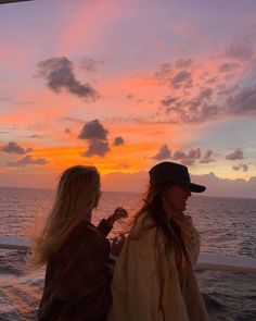 two women standing on the deck of a boat watching the sun set over the ocean