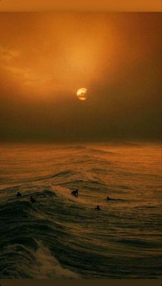 the sun is setting over the ocean with surfers in the water on their surfboards