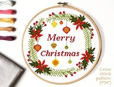 a cross stitch christmas wreath with poinsettis and holly on it, surrounded by other items