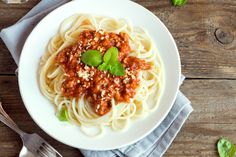 a white plate topped with pasta and sauce next to a cup of soup on top of a wooden table