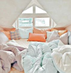 an unmade bed with many pillows and blankets on top of it in front of a window