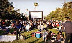 a large group of people sitting on top of a lush green field next to a movie screen