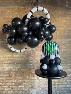 some black and white balloons are hanging on a brick wall with a balloon sculpture in the middle