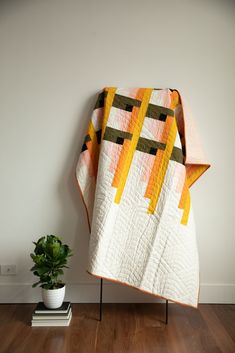 an orange and yellow quilt sitting on top of a wooden floor next to a potted plant