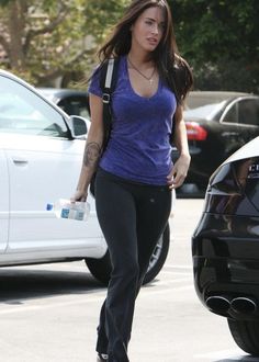 a woman walking across a parking lot next to parked cars