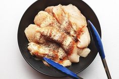 a black plate topped with chicken and seasoning next to a blue handled spatula