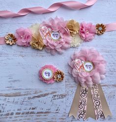 some pink and gold flowers are sitting on a white wooden table next to two ribbons