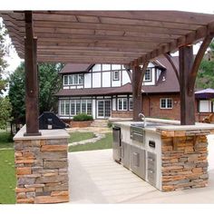 an outdoor kitchen and grill area under a pergolated patio with stone pillars, covered by wooden posts