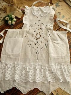 an old fashioned white dress is laying on the floor next to some papers and flowers