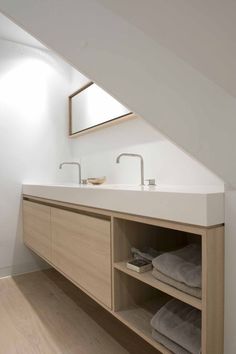 a bathroom with two sinks under a slanted window and wooden cabinets underneath the stairs