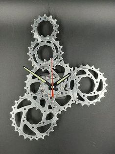 a clock made out of bicycle parts on a gray surface with red hands and numbers