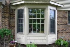 a white window sitting on the side of a brick building next to a green planter