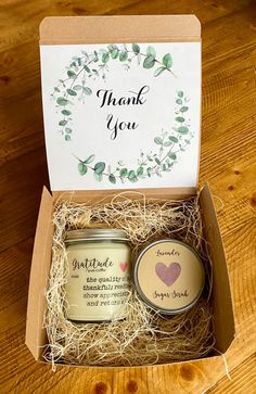 an open gift box with two candles and a thank card inside it on a wooden table