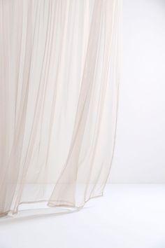 a cat sitting on top of a bed next to a white curtain with sheer drapes