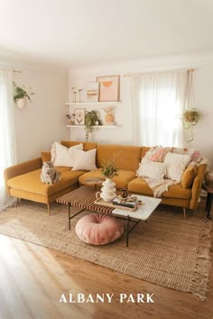 a living room with yellow couches and pillows on the floor in front of windows