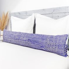 a white bed with blue and white pillows on it's headboard, next to a plant