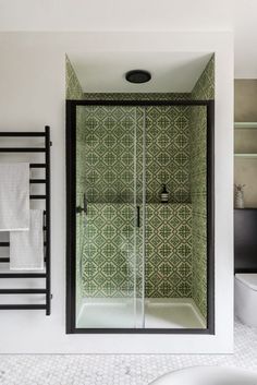 a bathroom with green and white tiles on the walls, shower stall and toilet in the corner