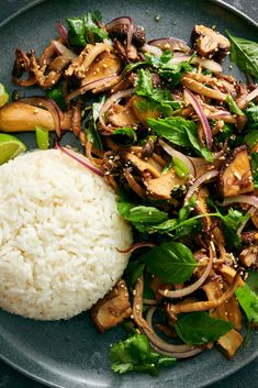 a plate filled with rice and vegetables on top of a wooden table next to a lime wedge