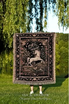 a woman standing in front of a tree holding up a tapestry with a horse on it