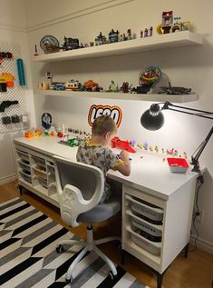 a young boy sitting at a desk with legos on the shelves above him and playing with his toys