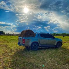 a truck with hay on the back parked in a field under a blue cloudy sky