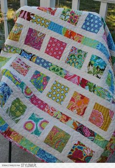 a colorful quilt sitting on top of a wooden chair next to a white fence and grass