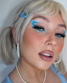 a woman with blue and white makeup looks at the camera while wearing pearls on her head