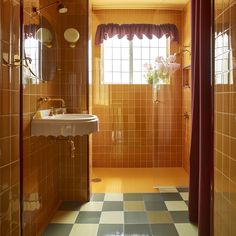 an orange tiled bathroom with a sink, shower and window in the corner is shown