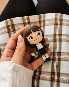 a person holding a small doll in their hand on top of a plaid cloth covered couch