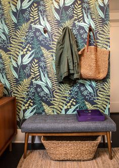 a bench in front of a wall with a plant pattern on it and a basket hanging from the back