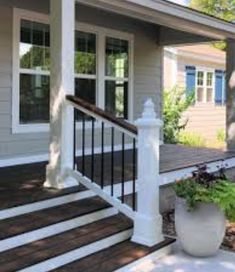 a porch with white railing and planters on the front steps, next to a gray house