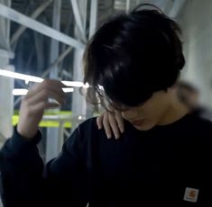 a woman in black shirt holding her hand up to her ear and looking down at the ground