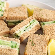 several sandwiches cut in half on a plate with lemons and cucumber slices