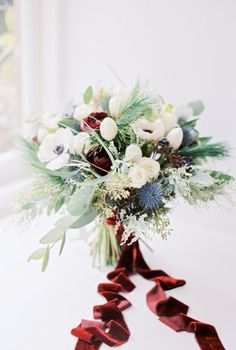 a bridal bouquet with red velvet bows and greenery on a table in front of a window