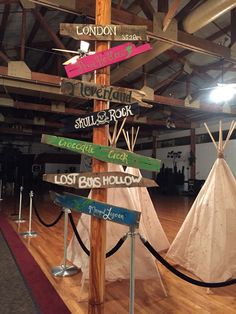 a pole with many signs on it in an indoor area next to a teepee tent