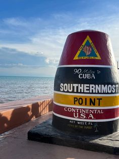 a large red and yellow sign sitting on the side of a road next to the ocean