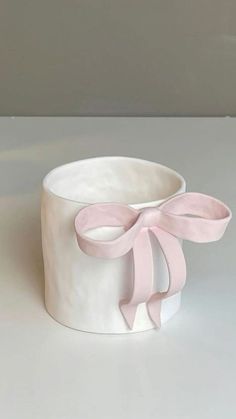 a white cup with a pink bow on the top and bottom, sitting on a table