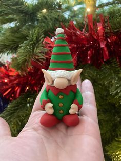 a small green and red elf figurine sitting in front of a christmas tree