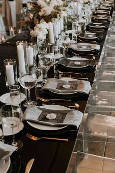 a long table is set with black and white place settings, silverware, and candles